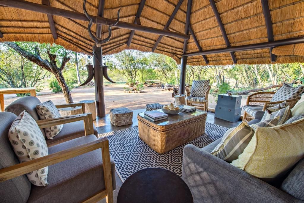 Lounge area with seating under a thatched roof, overlooking a natural landscape.