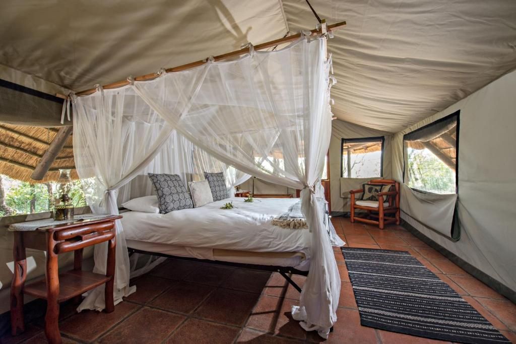 Safari tent interior with a bed draped in mosquito netting and a seating area.