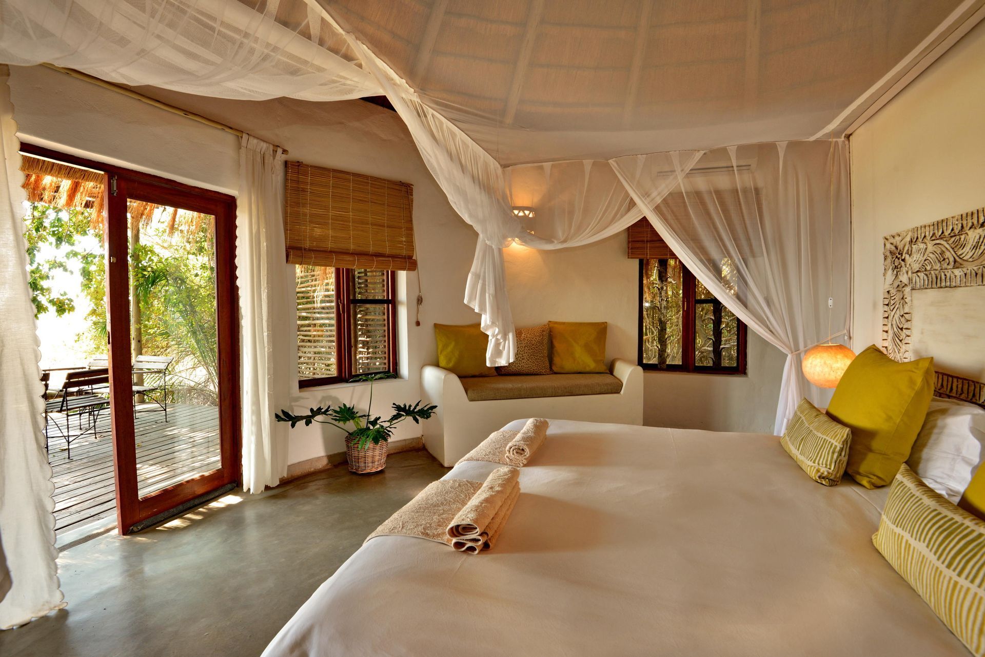 Bedroom with a large bed, mosquito net, built-in seating, and open doors to an outdoor balcony. 