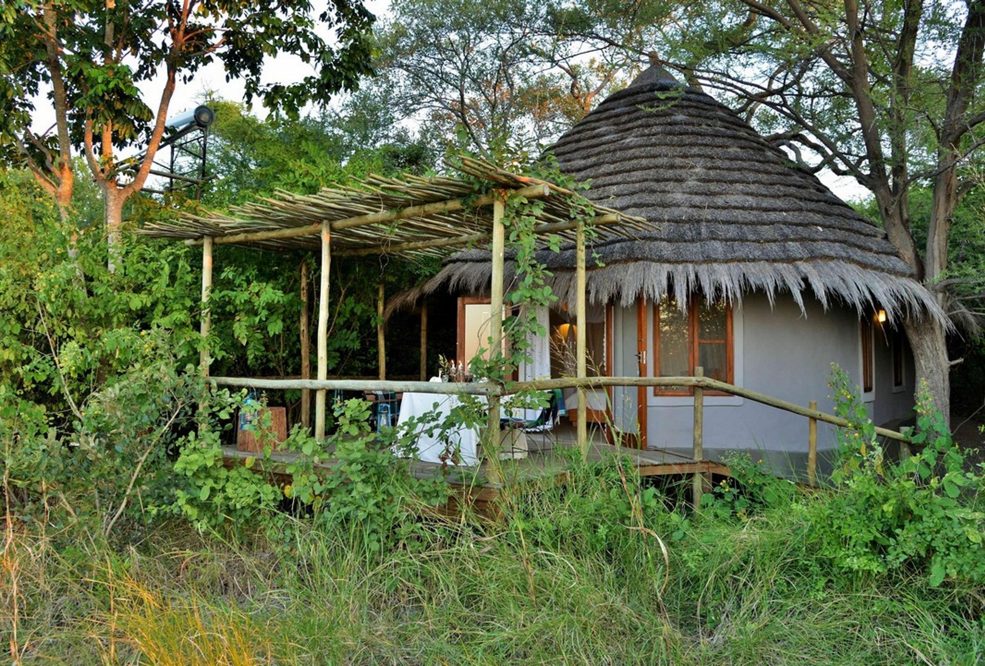 A round cabin with a thatched roof and porch, surrounded by greenery.
