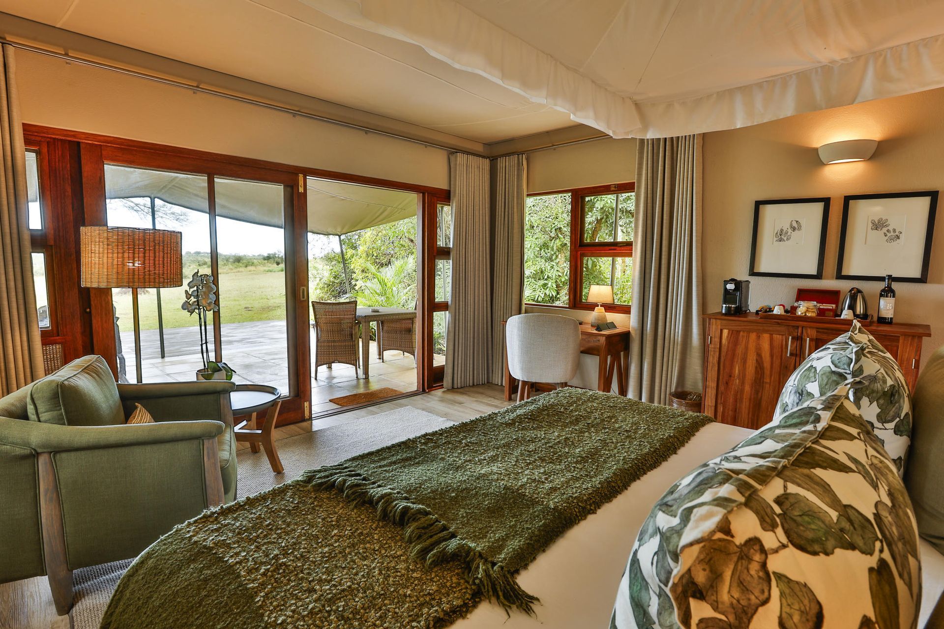 Cozy hotel room with a bed, armchairs, and a patio overlooking greenery.