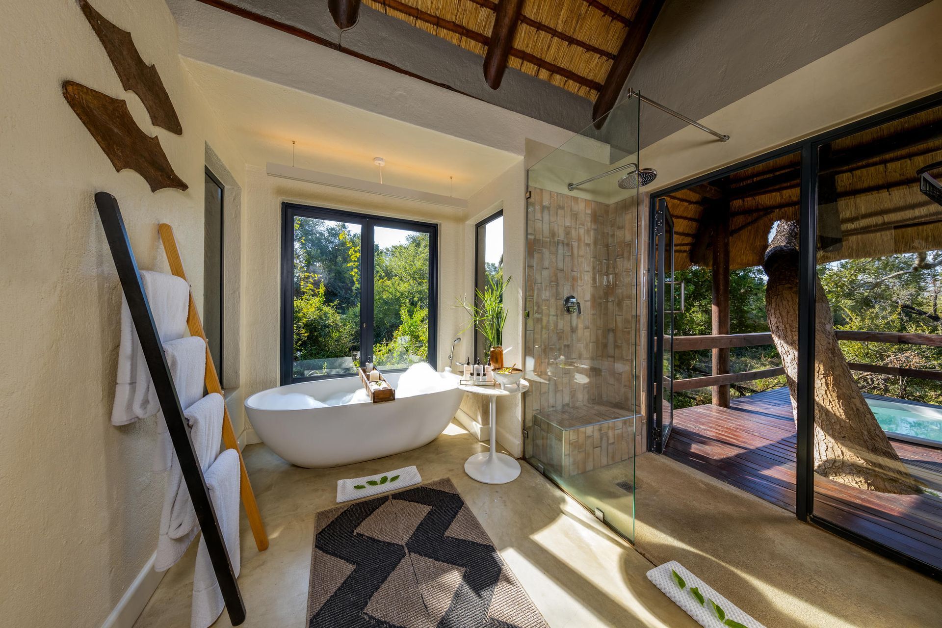 Bathroom with soaking tub, glass shower, and forest view; natural light and wood accents. Sabi Sabi LIttle Bush Lodge