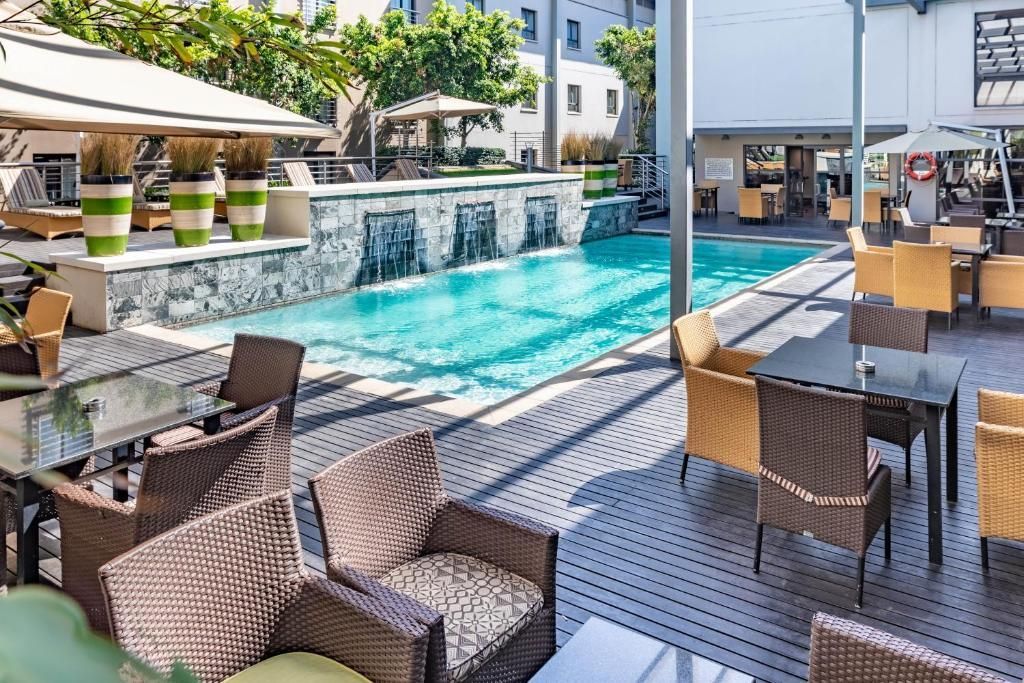 Outdoor restaurant seating area with pool. Wicker chairs, tables, waterfall, sunny day.