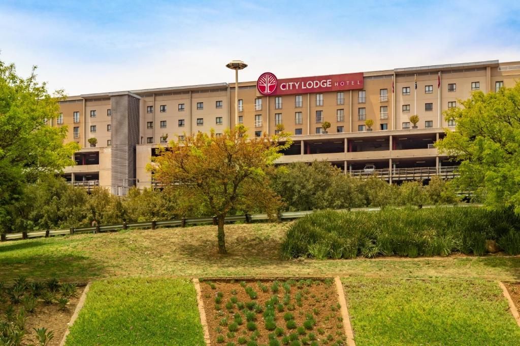 City Lodge Hotel with a red sign, behind a green grass lawn.