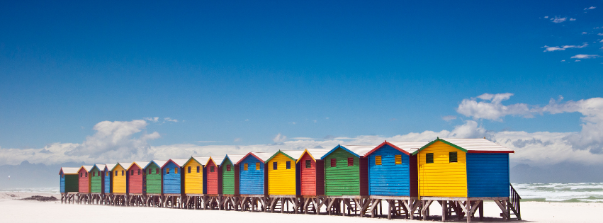 Colorful beach huts lined up along a sandy beach under a clear blue sky.
