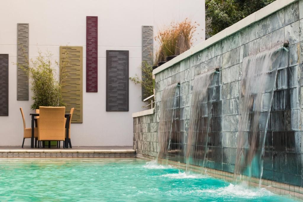 Pool with waterfall feature; outdoor dining area with decorative wall art.