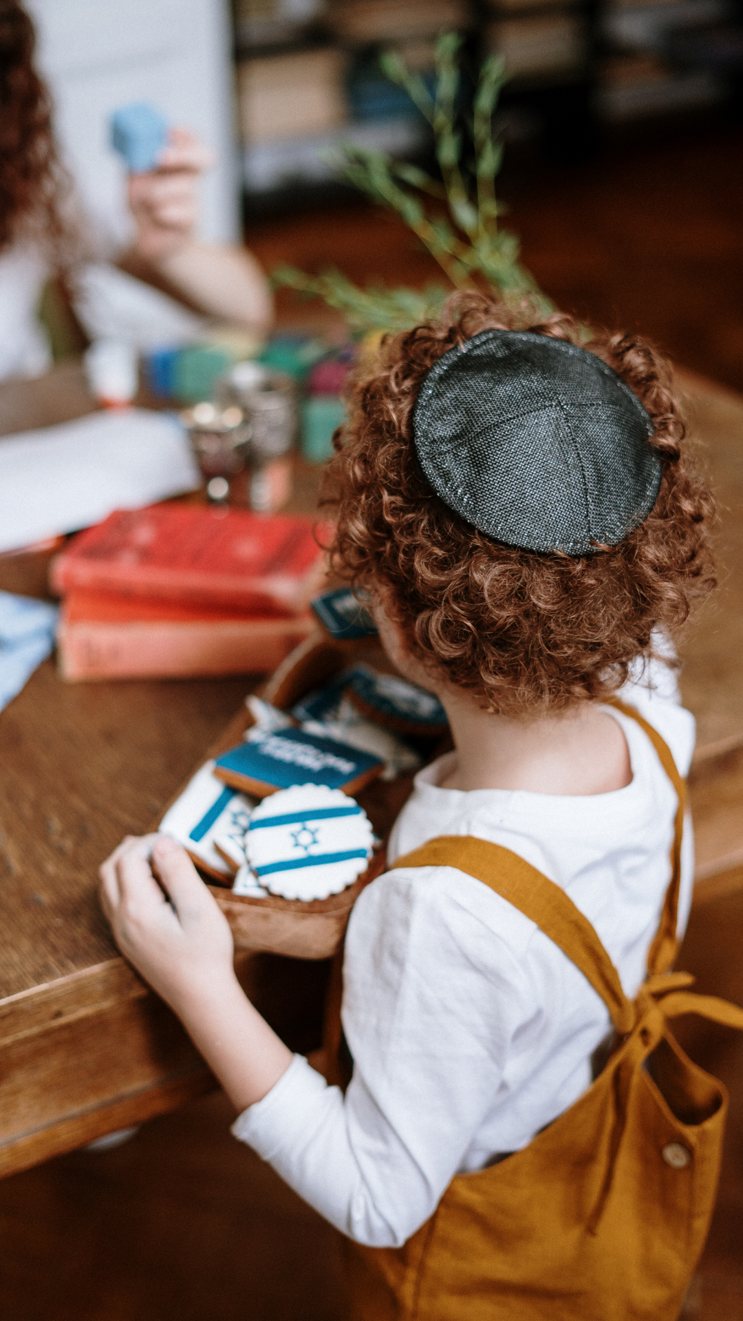 A child wearing a yarmulke and overalls holds a tray of cookies with Israeli flags on them.