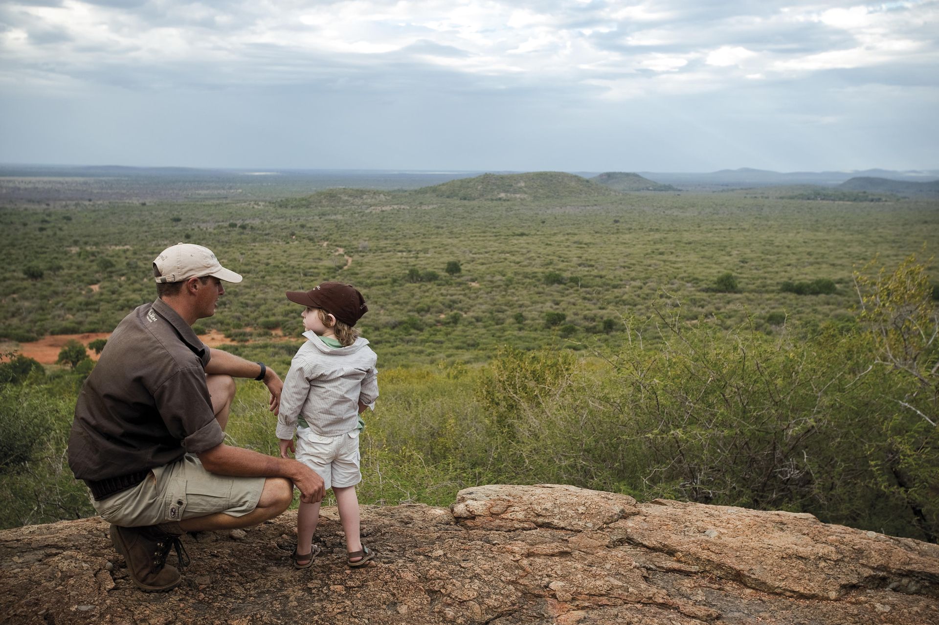 A man and a child are looking out over a lush green landscape. Family Friendly Safari