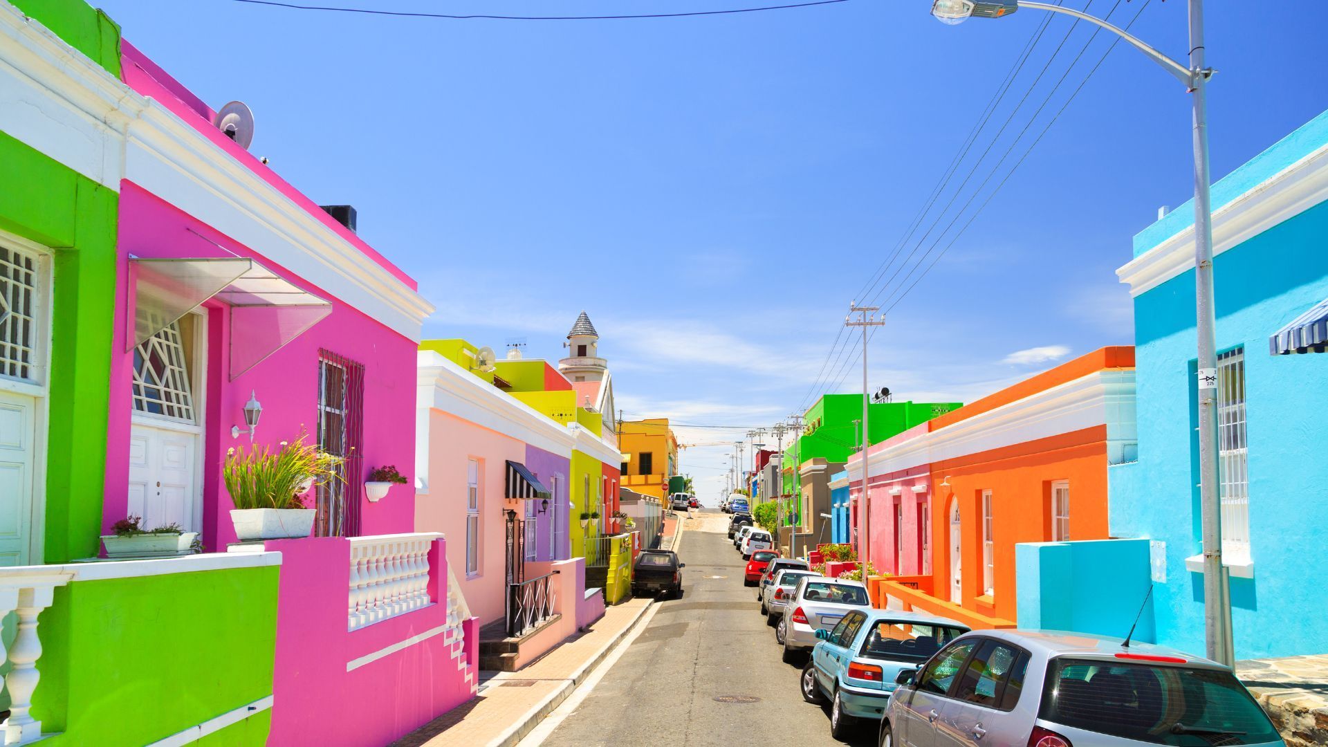Colorful houses line a street in Bo-Kaap, Cape Town, South Africa, under a clear blue sky.