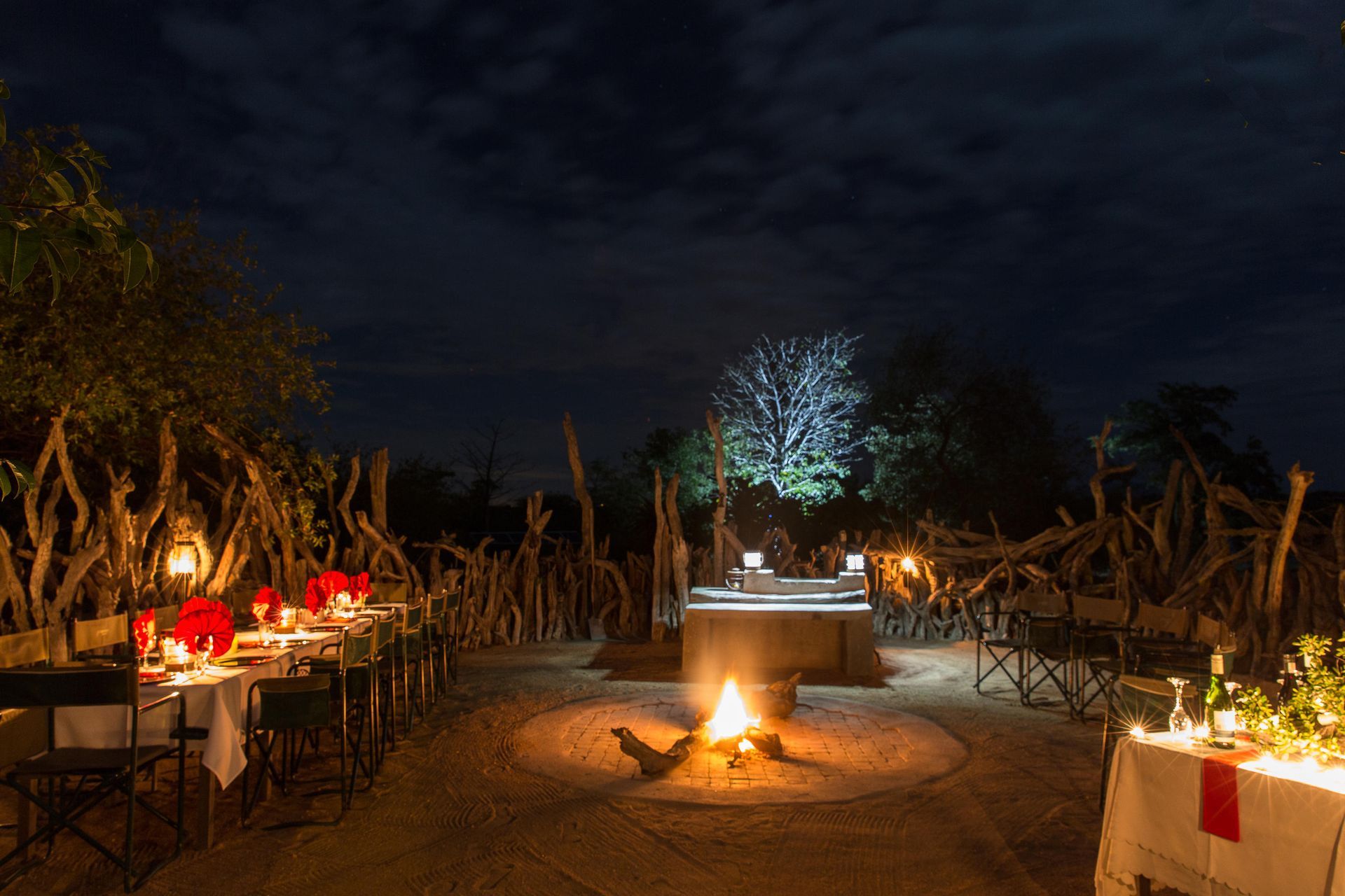 Nighttime outdoor dining setting with a bonfire. Tables set for dinner.