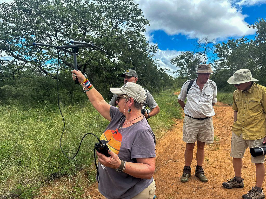Woman operates equipment in a field with three observers. She holds a device aloft, the others watch attentively.