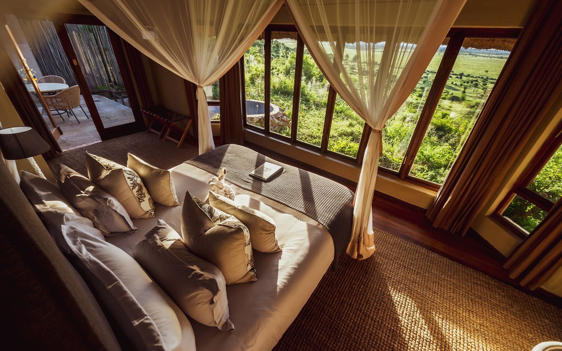 Bedroom with large windows overlooking a lush, green landscape; bed has cream pillows, draped with netting.