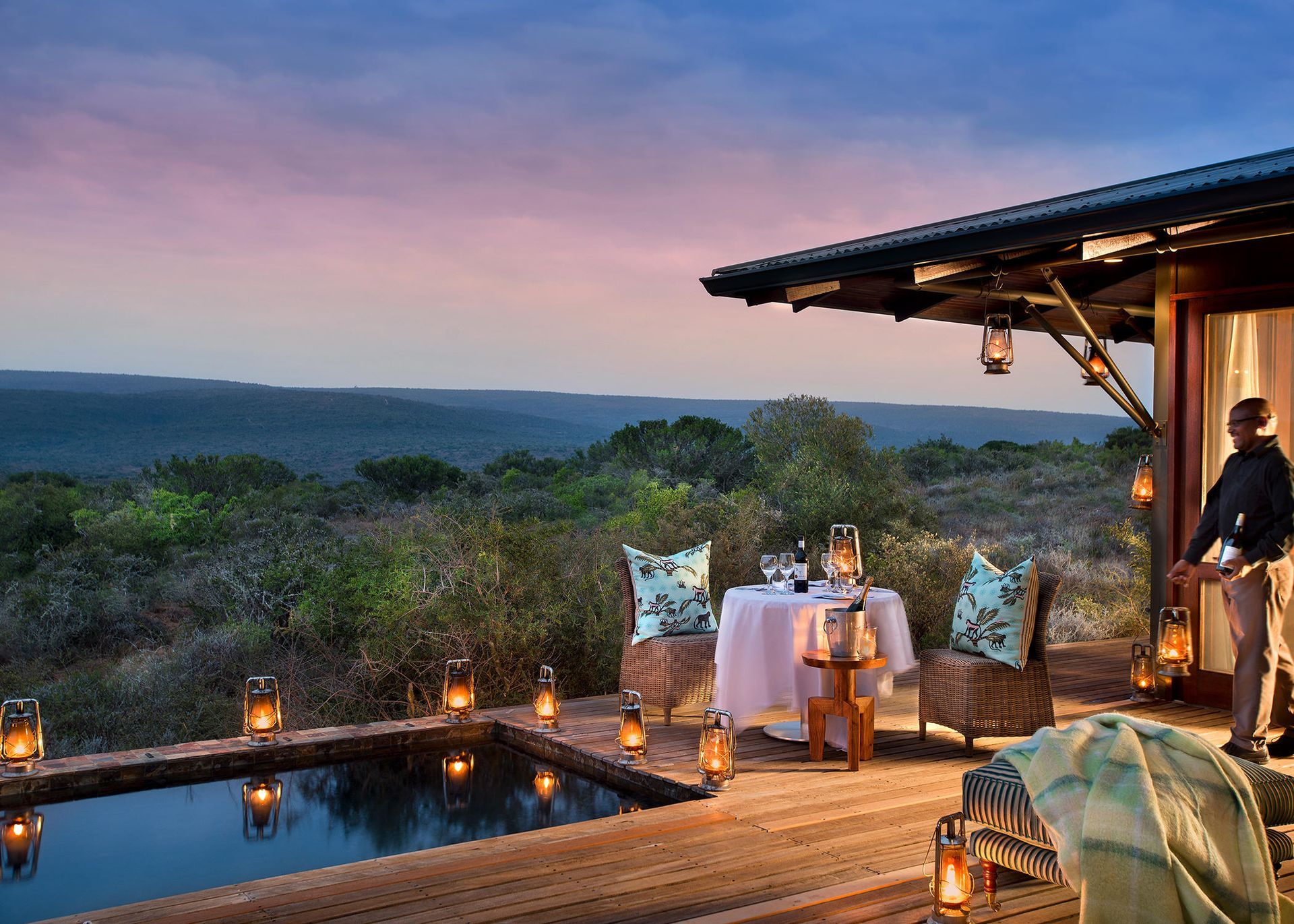 A man is standing outside of a house with a table and chairs in front of a pool. Malaria Free Safari Destinations