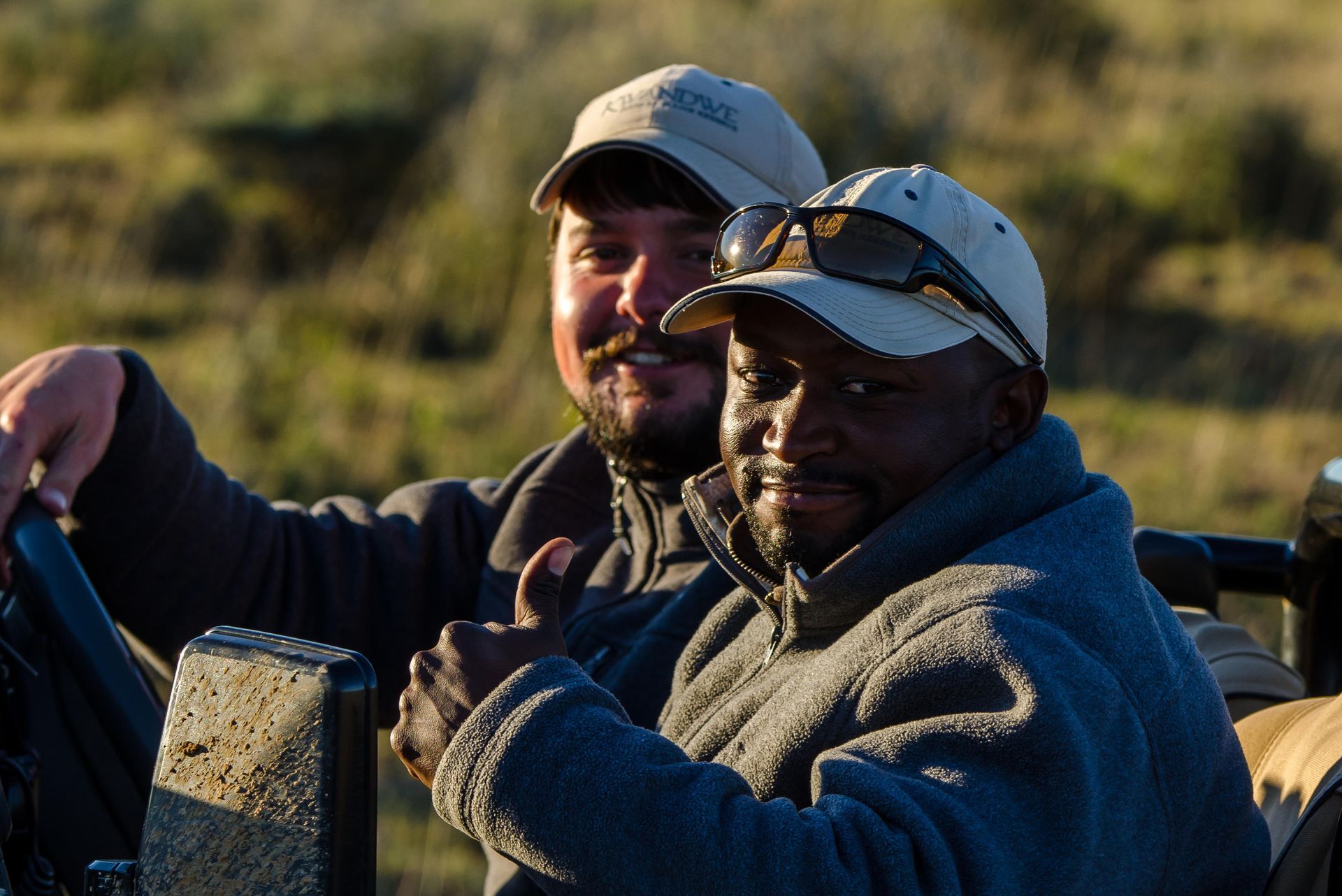 Two men wearing hats and sunglasses are sitting in a vehicle. Malaria Free Safari Destinations