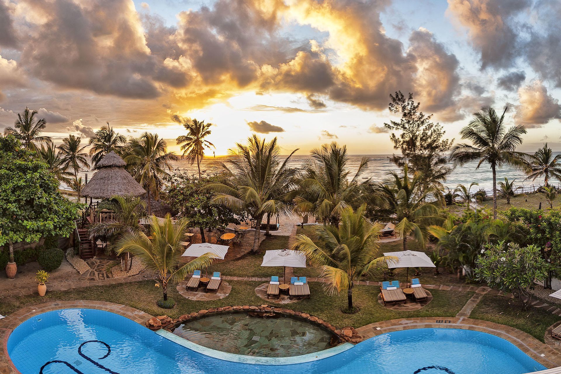 Woman setting a table with food and drinks on a beach with ocean in the background.