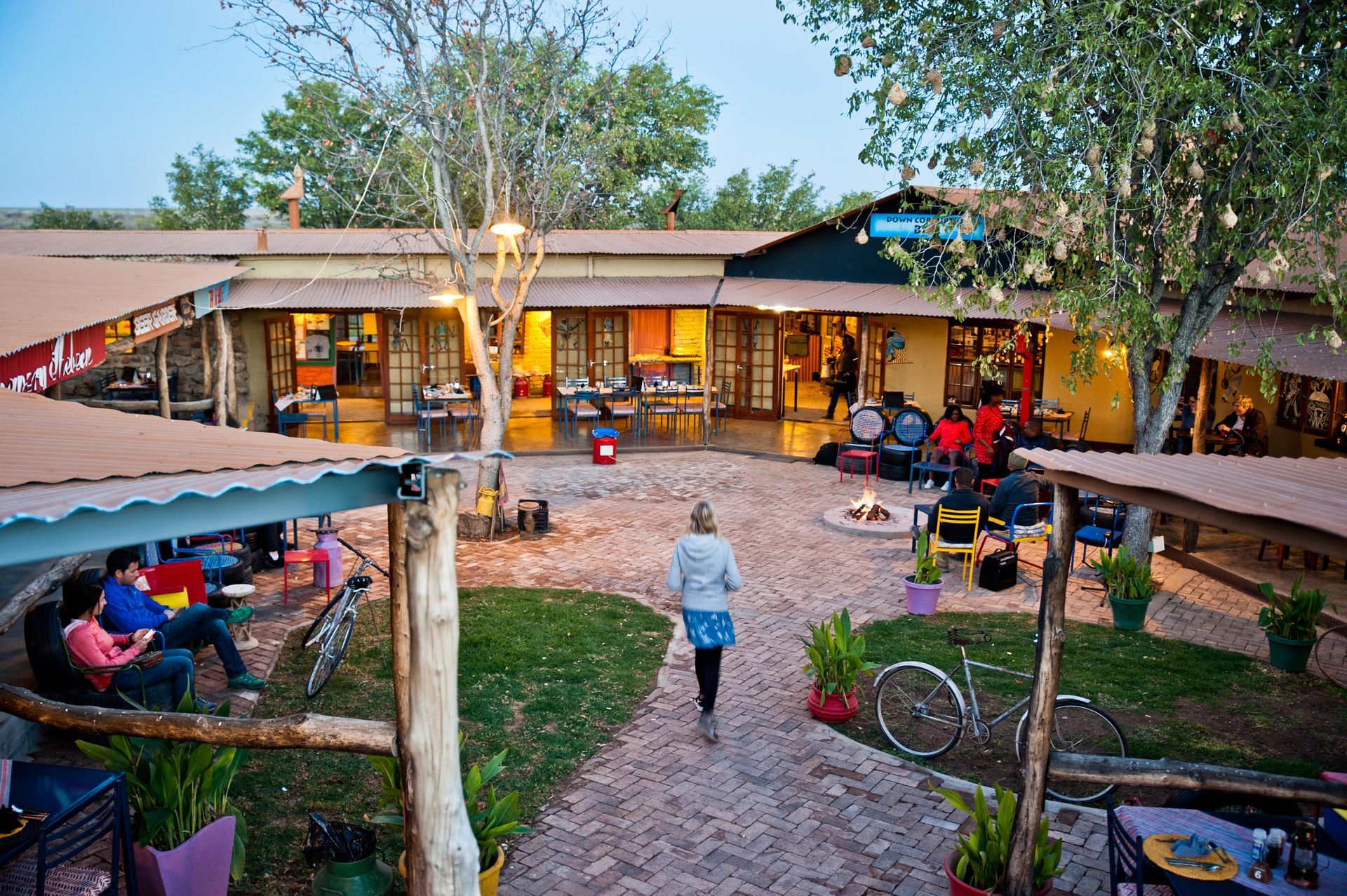 Courtyard with people, a building, and a small fire pit. Trees and seating areas are present.