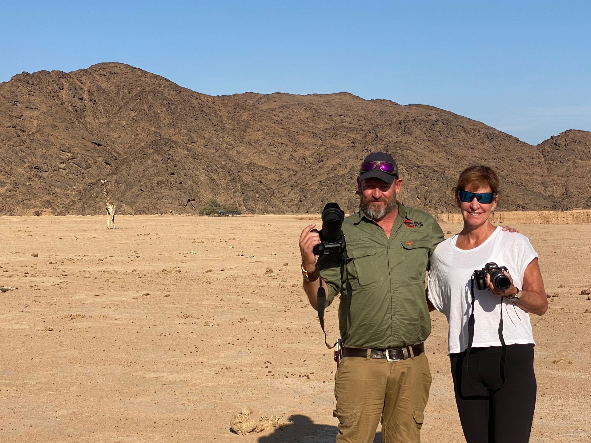 A man and a woman are standing in the desert holding cameras. Namibia Safari