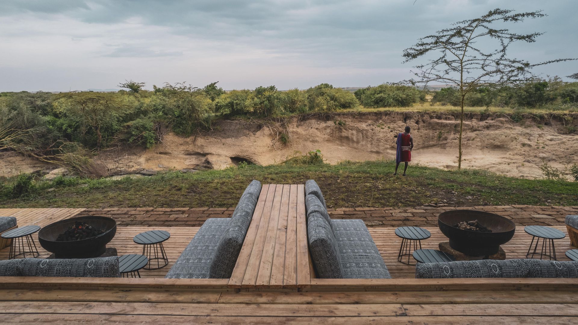 Wooden deck with seating overlooking an arid landscape. A person stands in the distance.