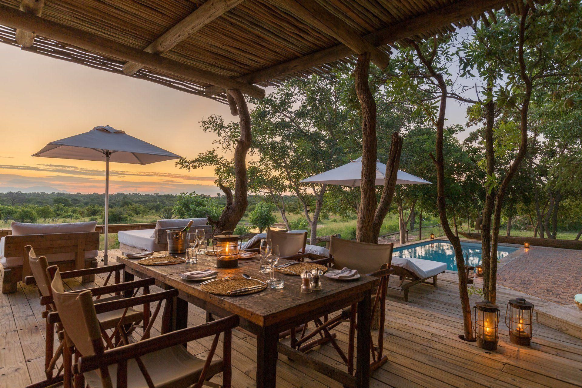Open-air lodge dining deck at sunset with wooden tables, lanterns, and a pool overlooking the landscape
