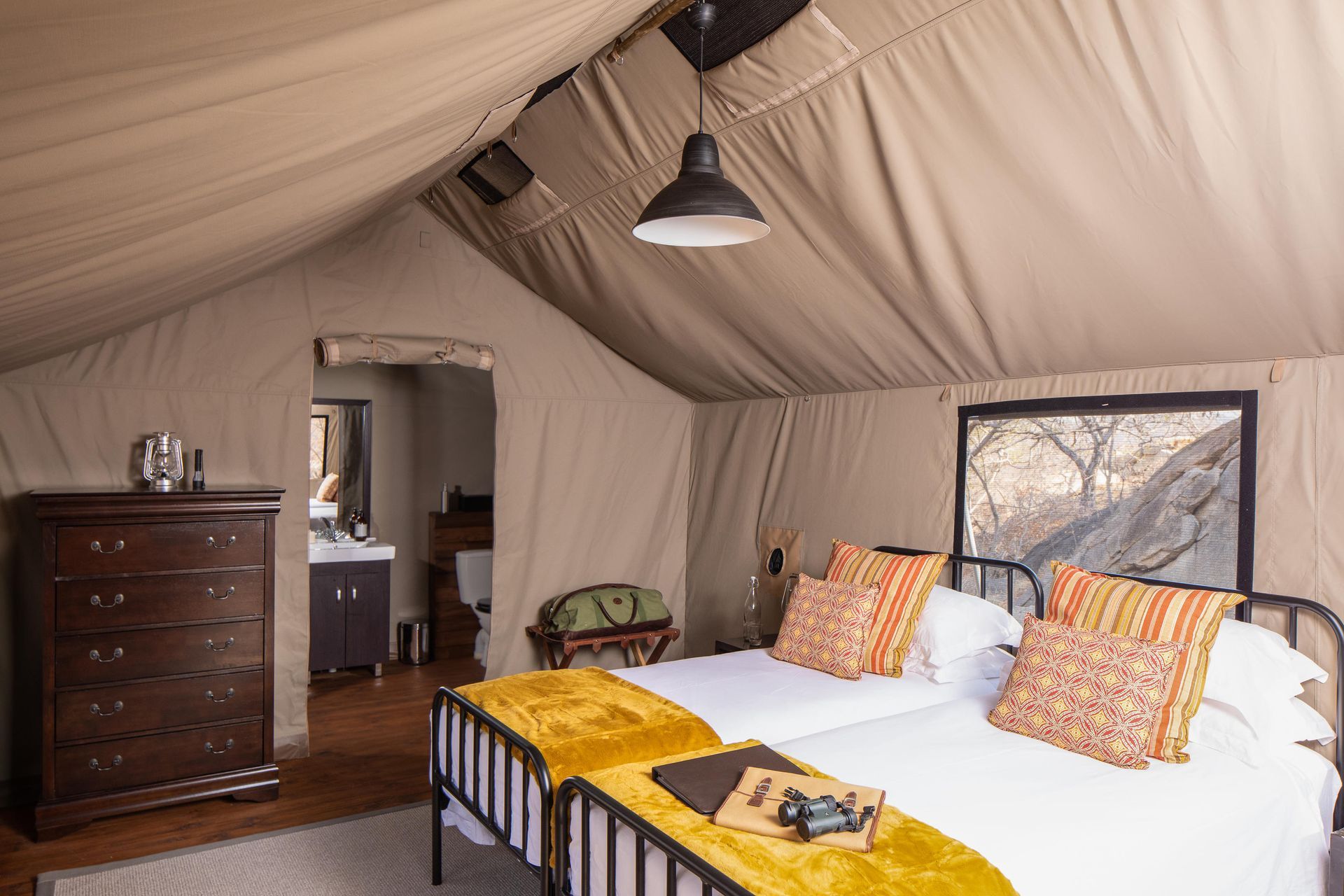 Safari tent interior with two beds, dresser, and en suite bathroom.