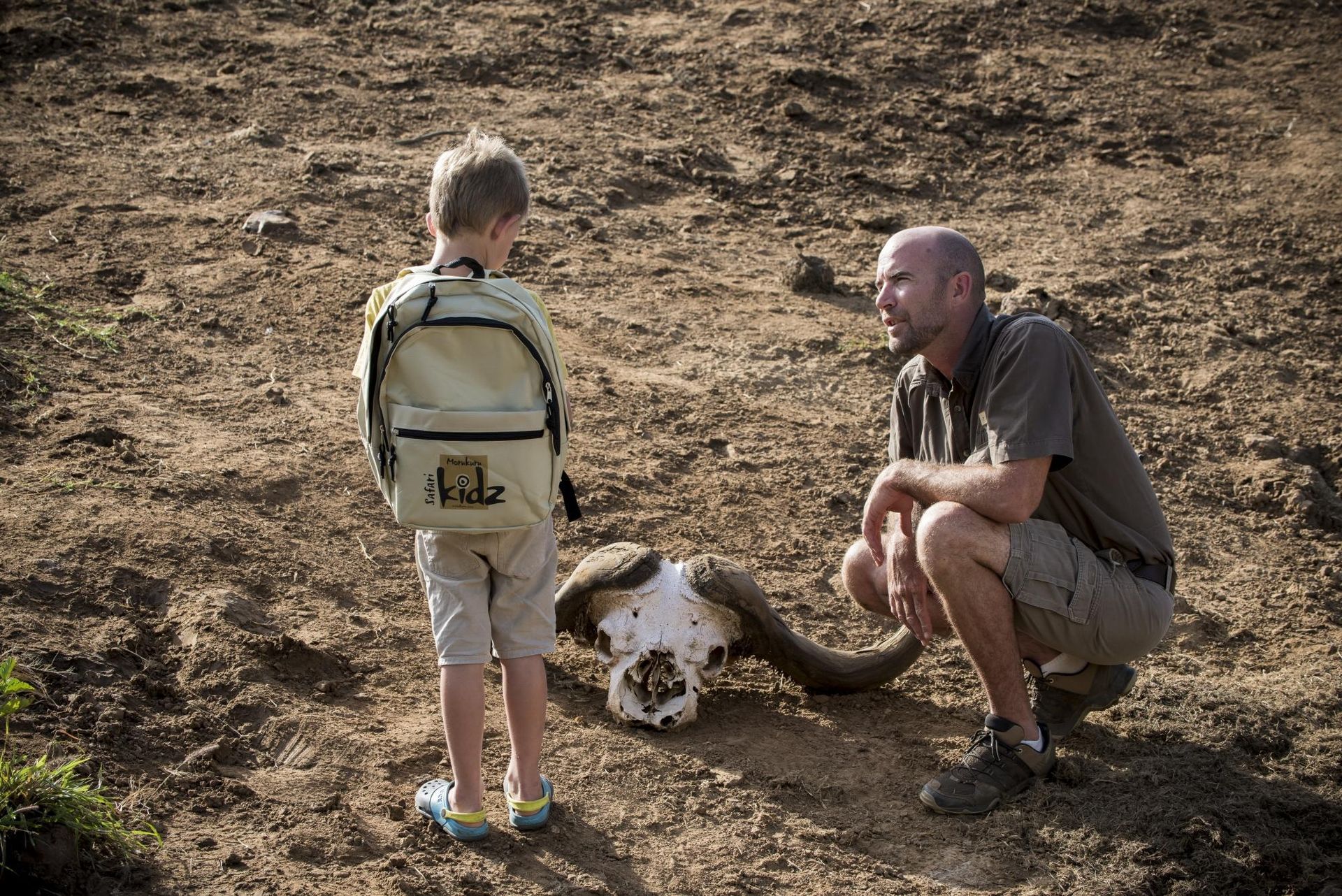A man and a boy are talking to each other in a dirt field. Malaria Free Safari Destinations