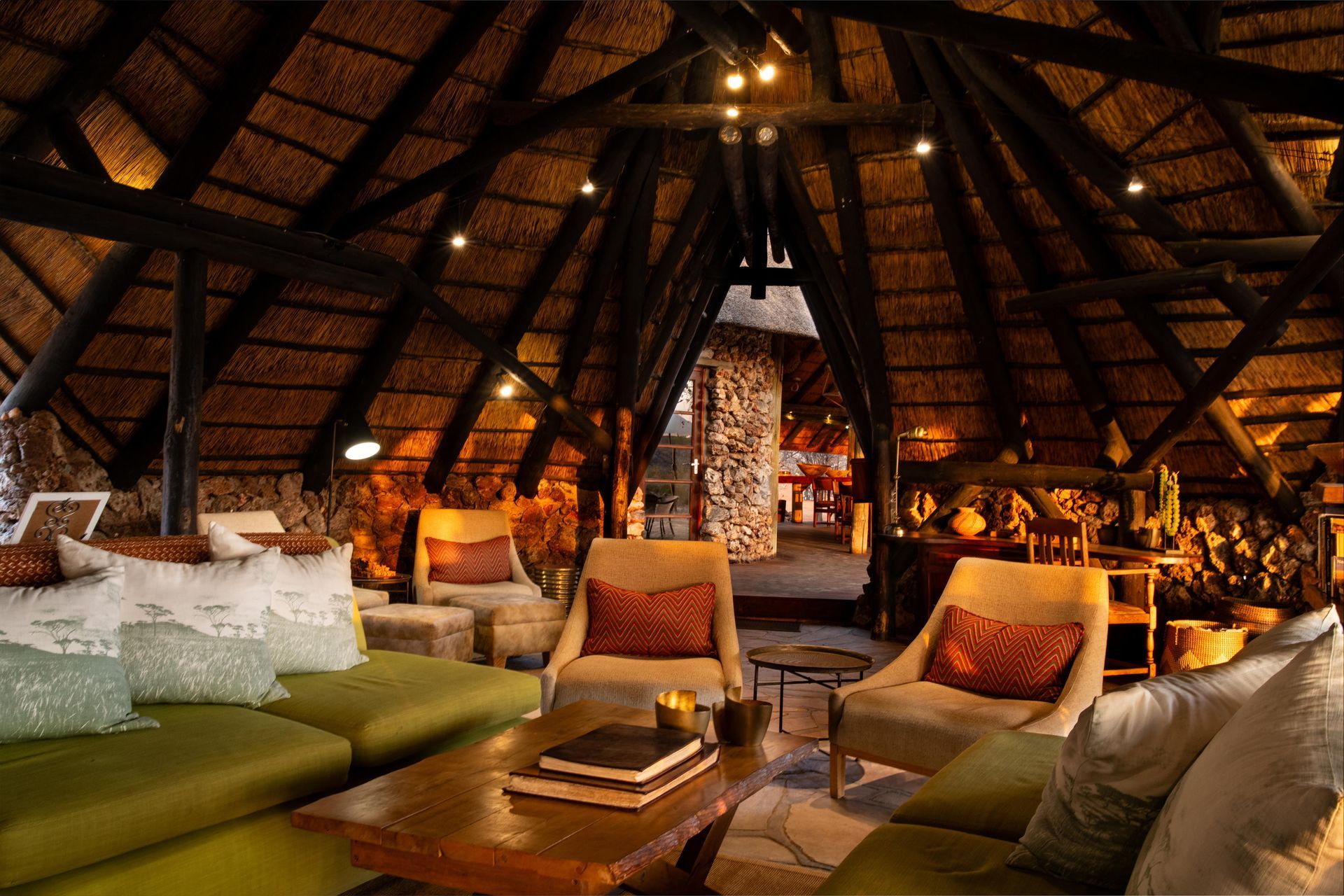 Cozy lounge with thatched roof, olive green sofa, beige armchairs, and coffee table.