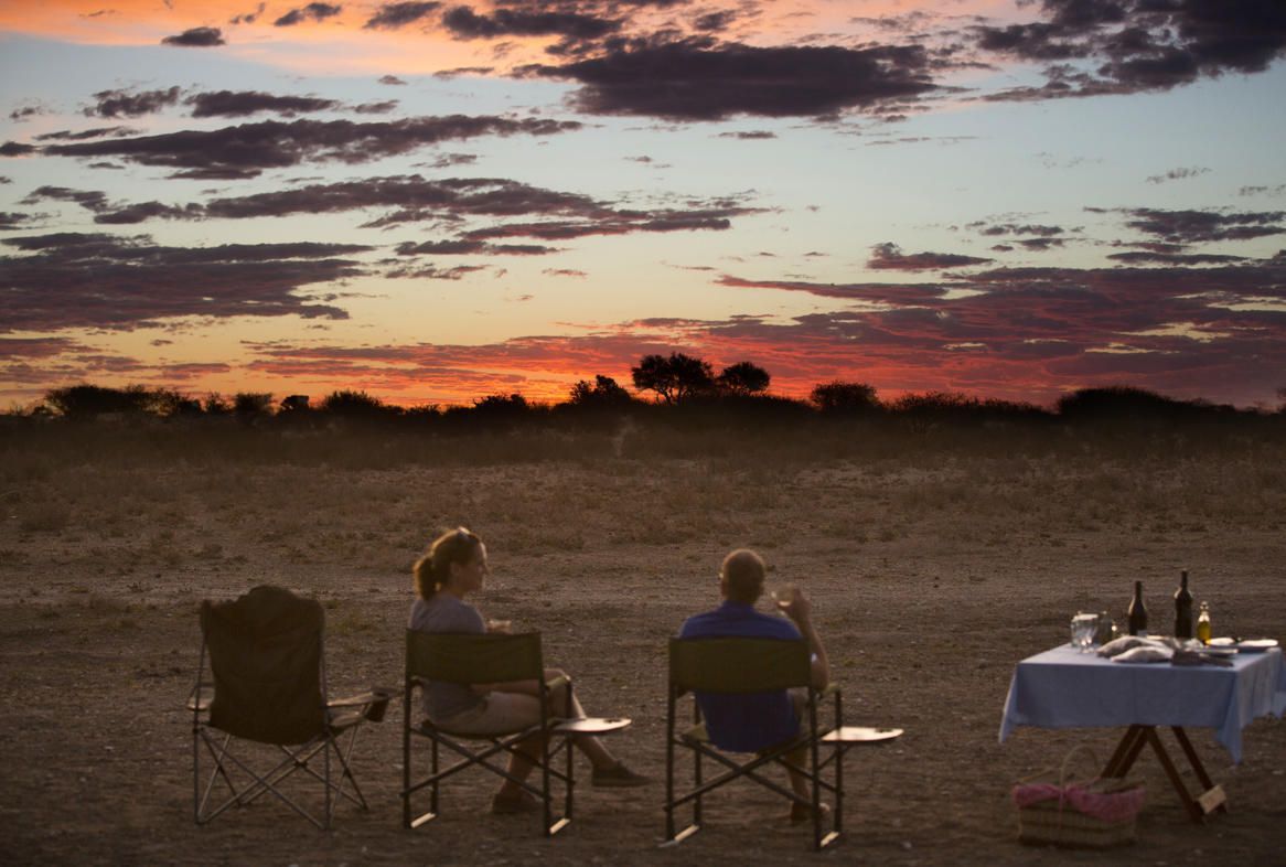 Two people are sitting at a table in the desert watching the sunset Malaria Free Safari Destinations
