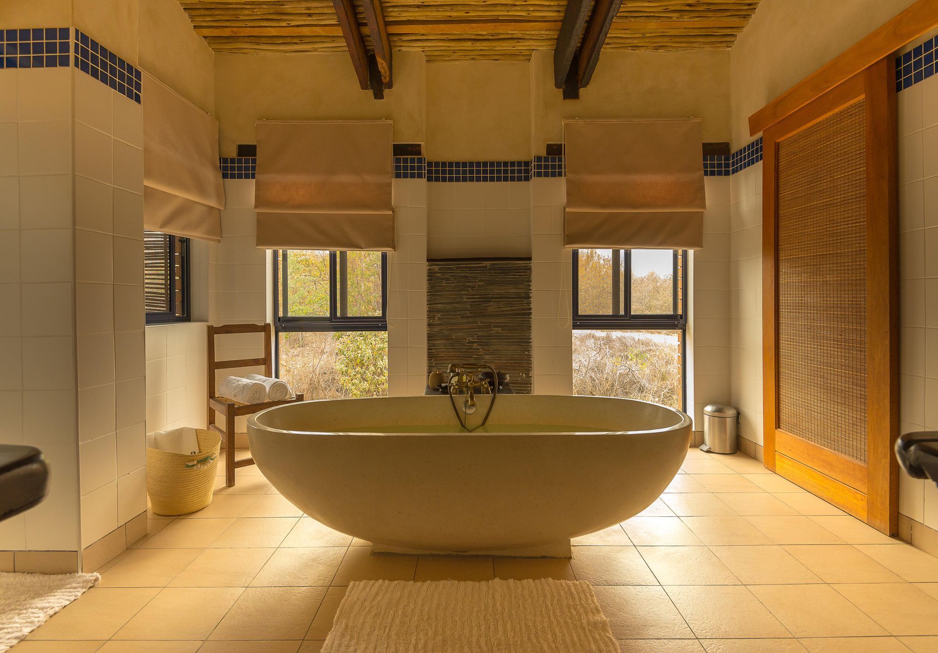 Spacious bathroom with a large, oval bathtub centered in front of two windows with a view. 