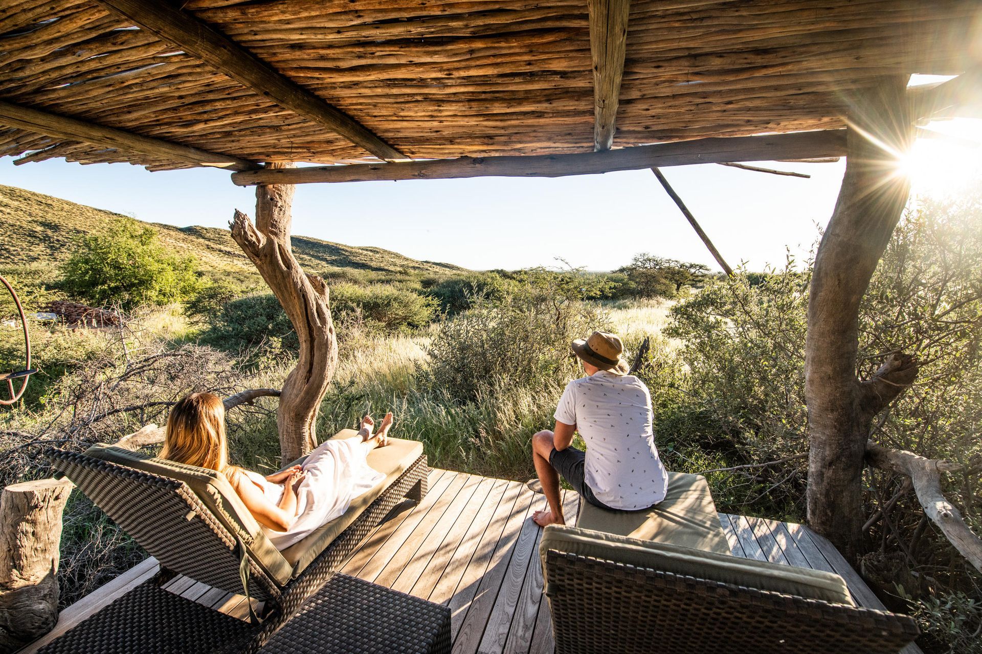 Couple relaxing on a deck overlooking a scenic landscape with sunshine.