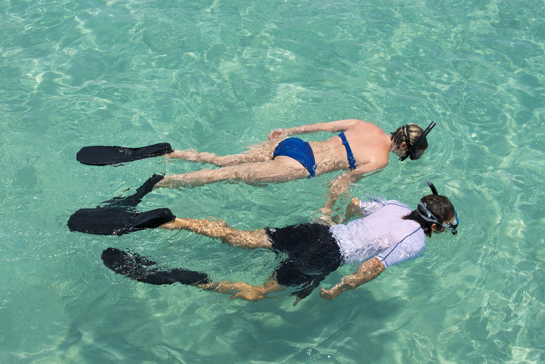 Two people snorkeling in clear turquoise water, wearing fins and masks.