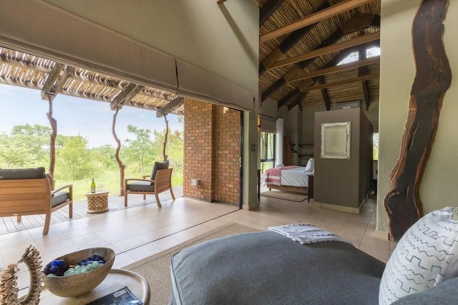 Interior of a luxury safari lodge room with open doors to a patio, showcasing a bed, seating, and natural elements.