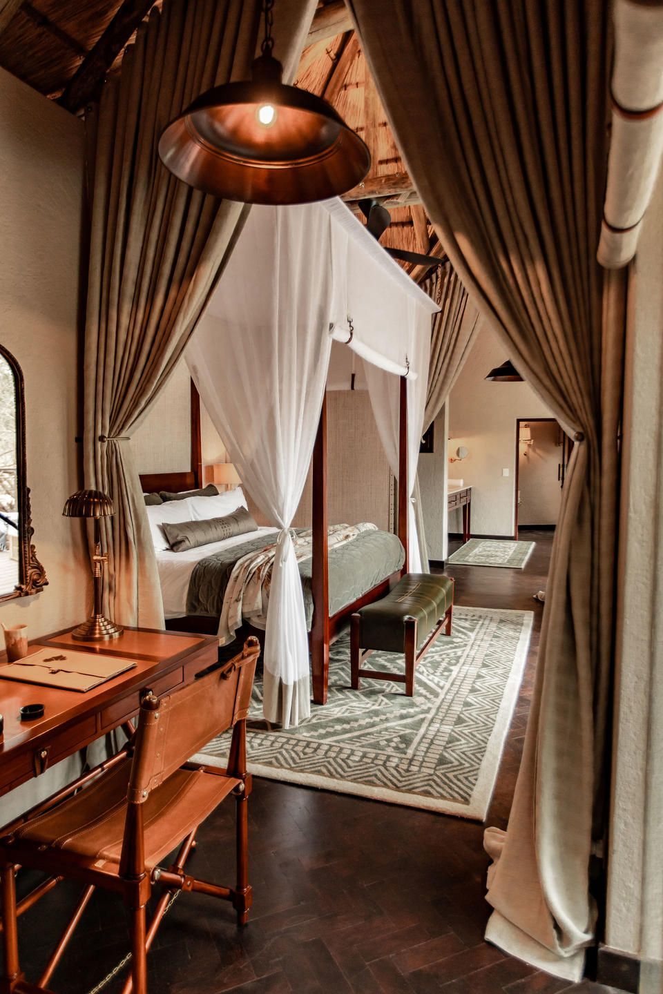 Luxurious bedroom with canopy bed, desk, and curtains in a lodge setting.