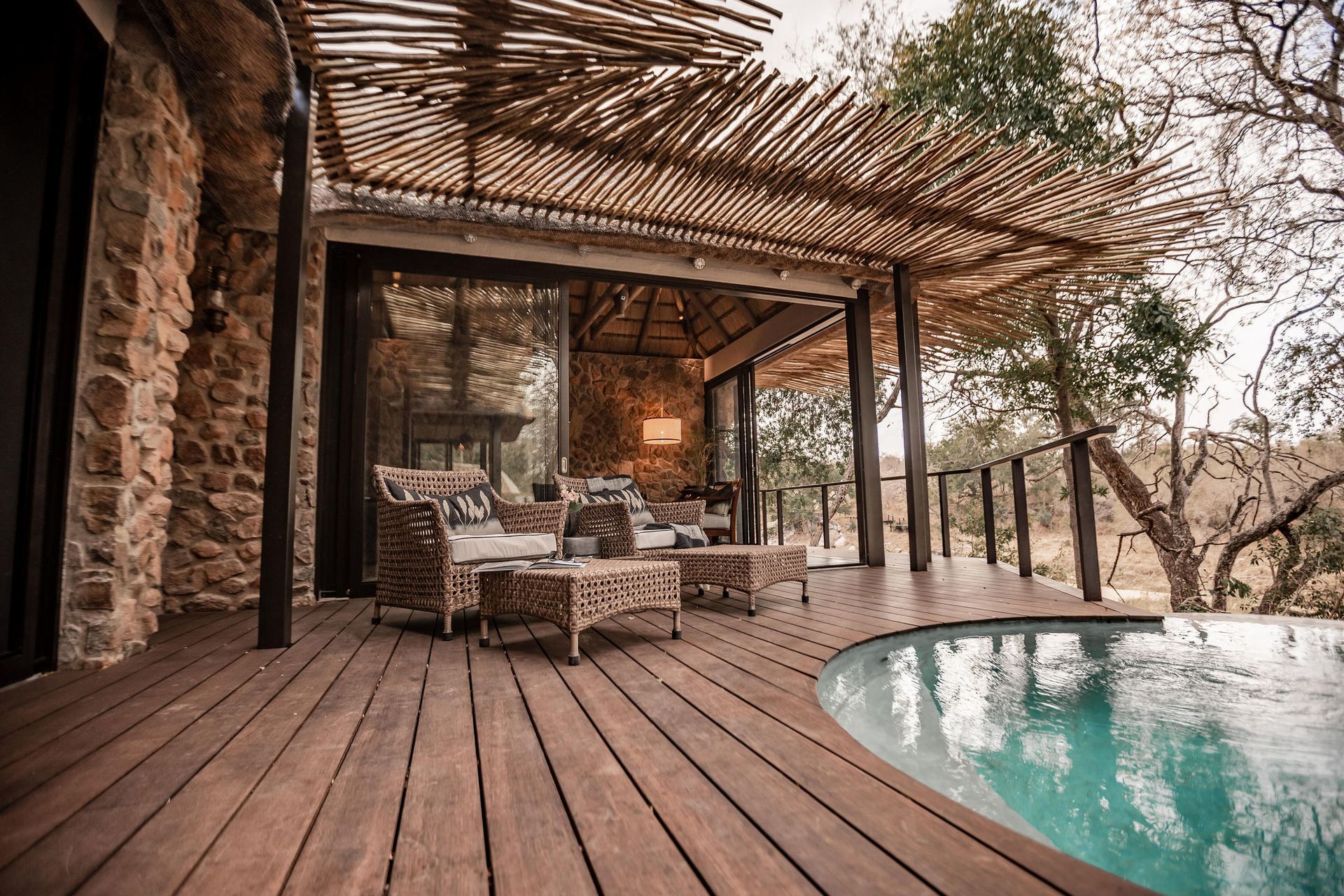 Wooden deck with a pool, open-air seating area, and stone wall building in a natural setting.