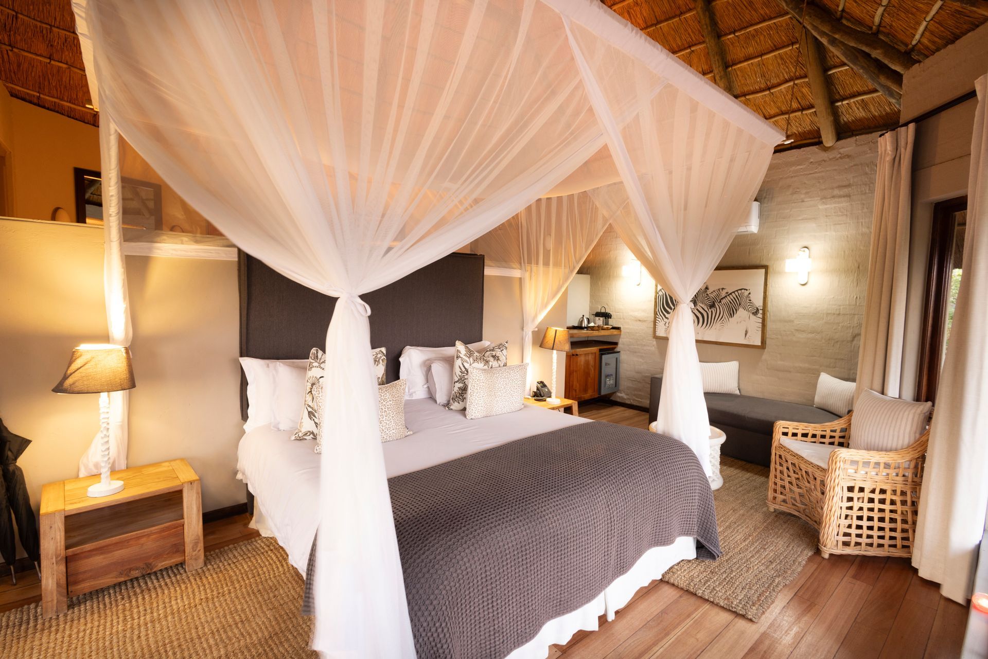 Bedroom with canopy bed, neutral tones, thatched ceiling, and wicker furniture.