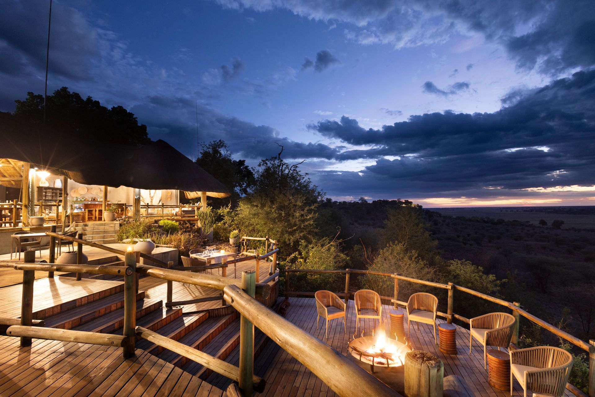 Wooden deck with fire pit and seating, overlooking landscape at dusk.