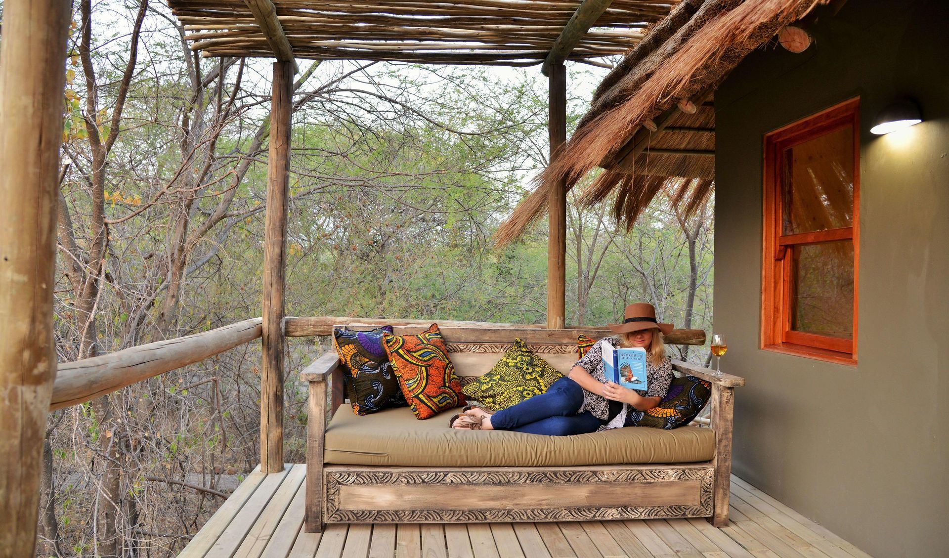 A woman is laying on a couch on a porch reading a book.