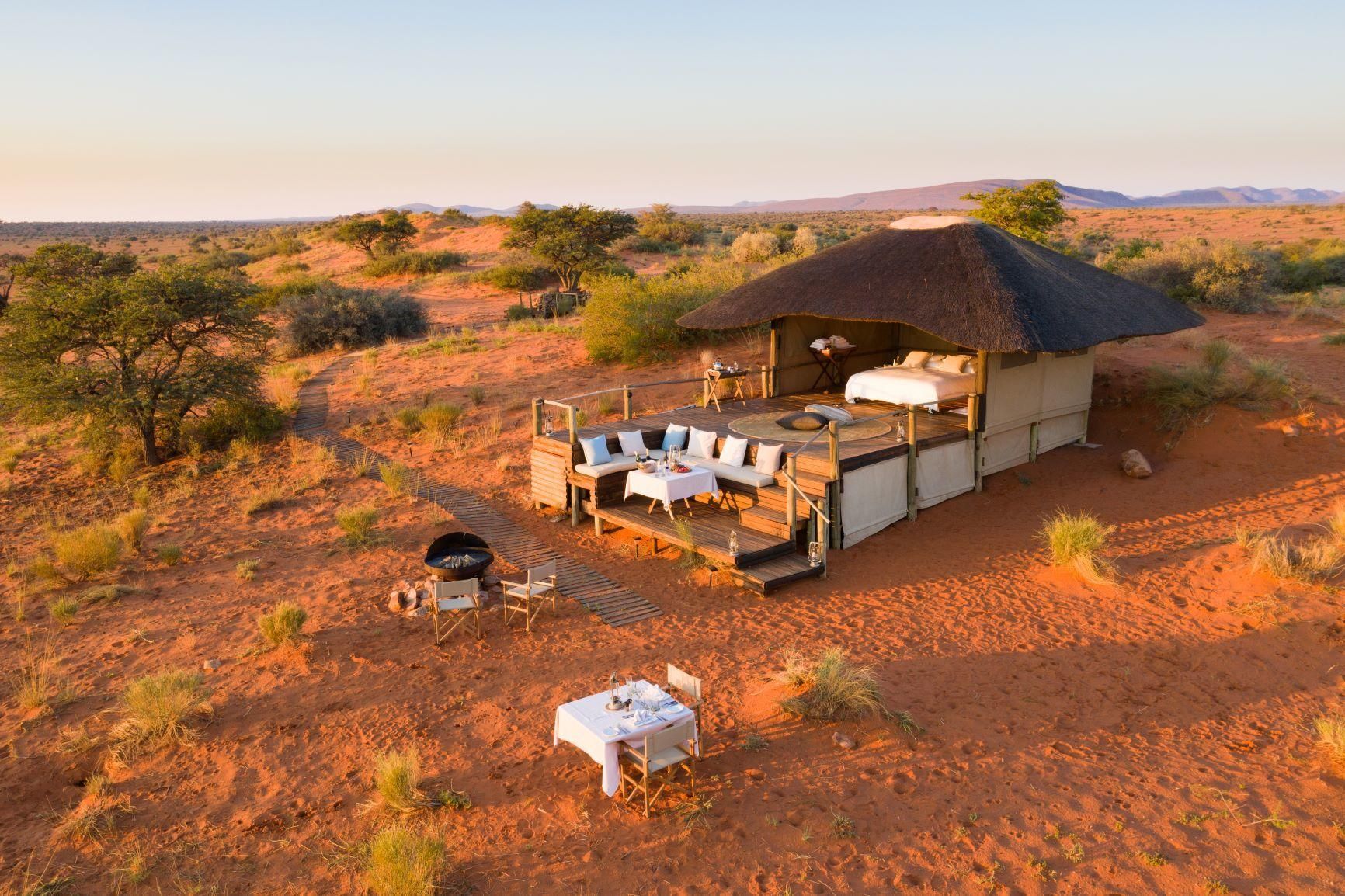 Safari lodge with a thatched roof and outdoor dining in a desert landscape at sunset.