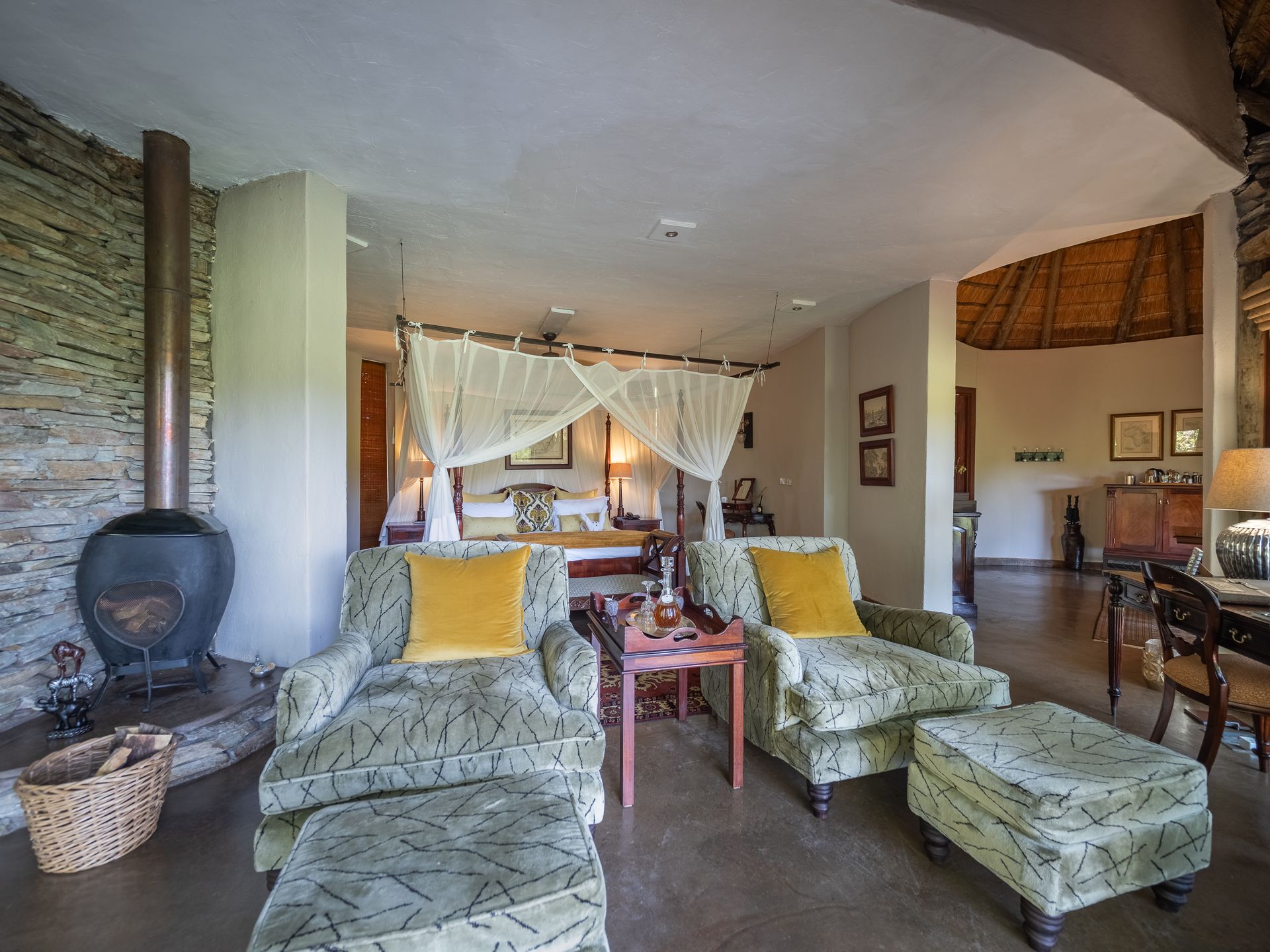 Cozy room with a four-poster bed, two armchairs with ottomans, a fireplace, and a doorway to another room.