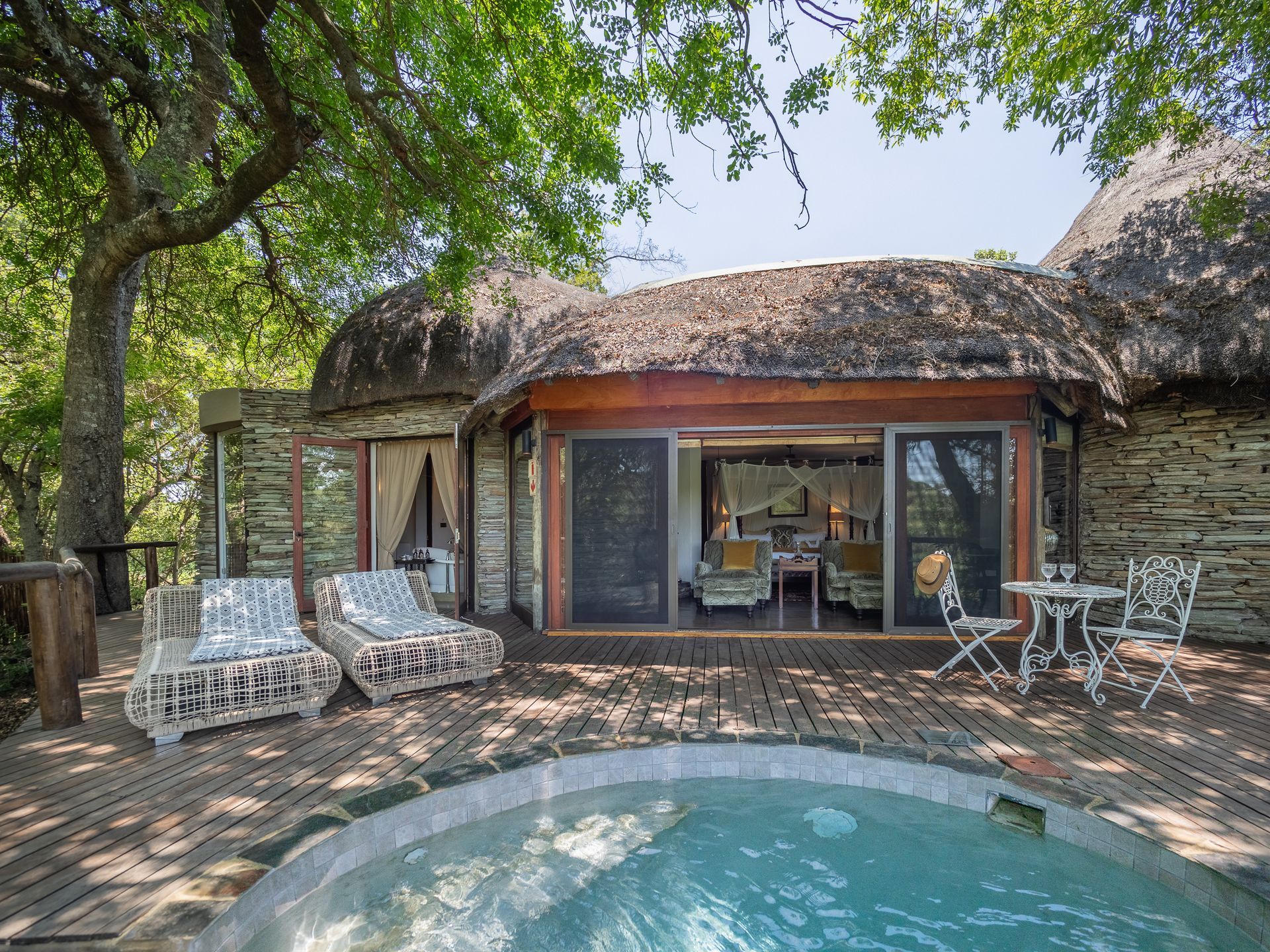 A thatched-roof bungalow with a private pool, outdoor seating, and a view of the interior.