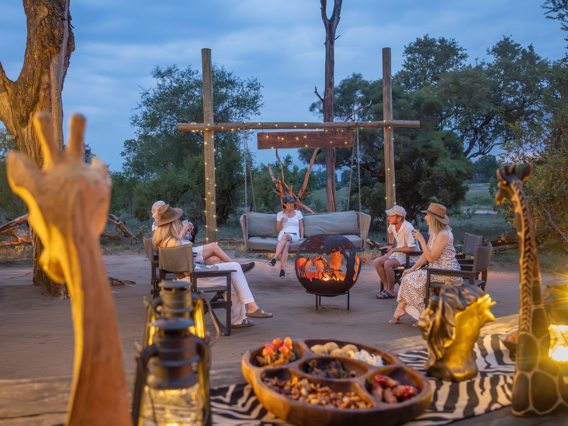 Group of women around a fire pit on safari, enjoying snacks and conversation.