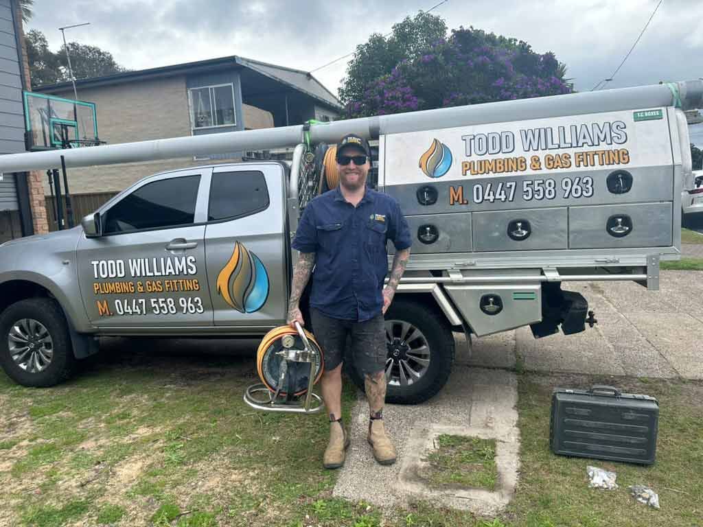 A Man Is Standing In Front Of A Truck — Todd Williams Plumbing and Gas Fitting In Forster, NSW