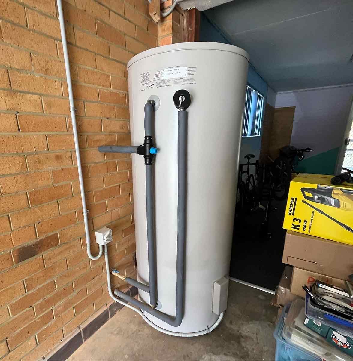 A White Water Heater Is Sitting Next To A Brick Wall — Todd Williams Plumbing and Gas Fitting In Forster, NSW