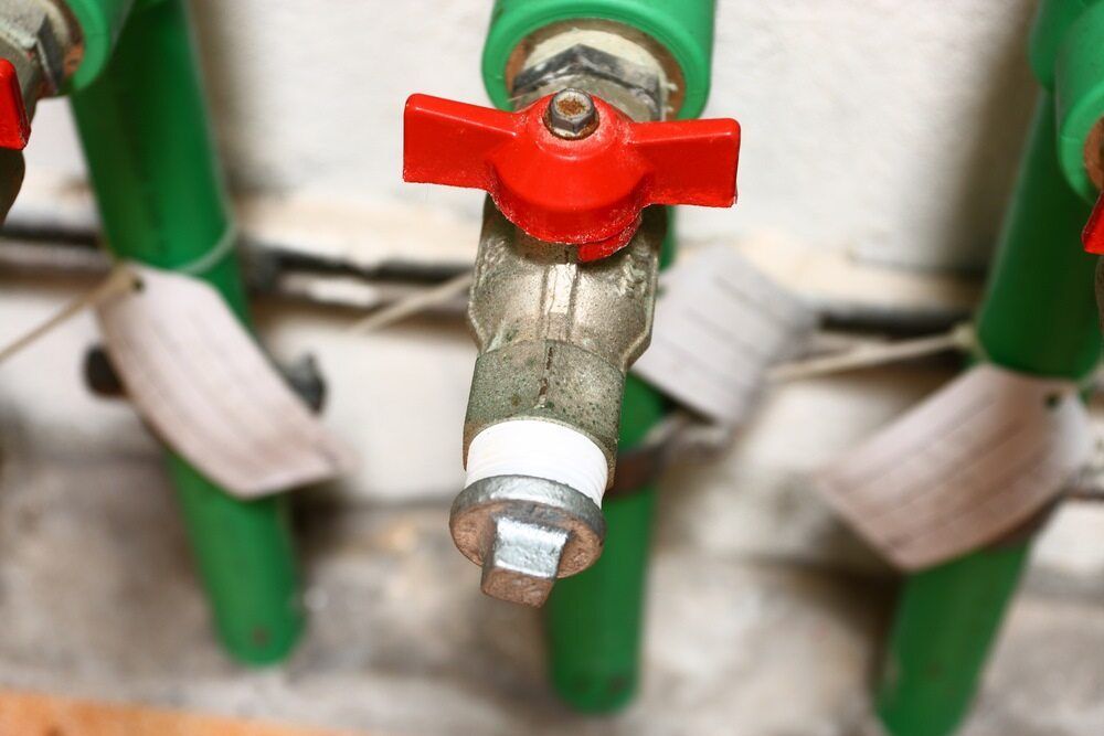 A Close Up Of A Faucet With A Red Handle On A Green Pipe — Todd Williams Plumbing and Gas Fitting In Forster, NSW
