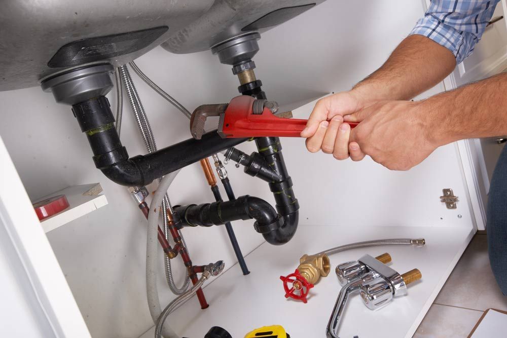 A Man Is Fixing A Sink With A Wrench — Todd Williams Plumbing and Gas Fitting In Forster, NSW