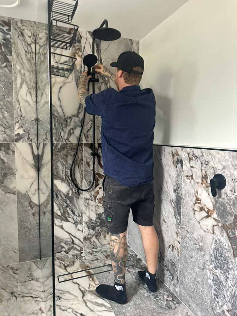 A Man Is Fixing A Shower Head In A Bathroom — Todd Williams Plumbing and Gas Fitting In Forster, NSW