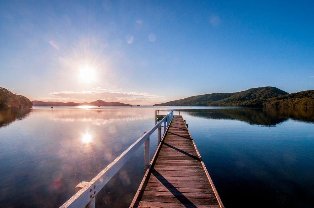 A Wooden Dock Leading Into A Lake At Sunset — Todd Williams Plumbing and Gas Fitting In Pacific Palms, NSW