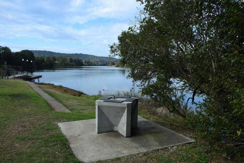 A Concrete Table Is Sitting On The Shore Of A Lake — Todd Williams Plumbing and Gas Fitting In Wingham, NSW