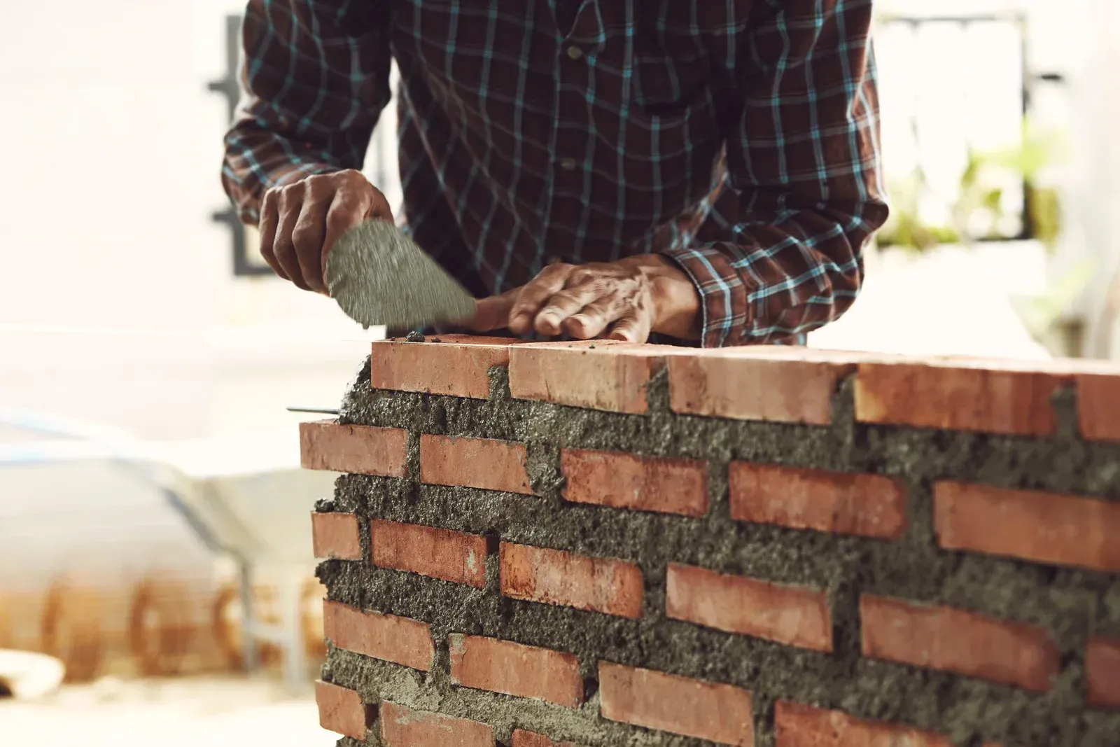 Worker laying bricks on a wall with mortar in a bright construction site