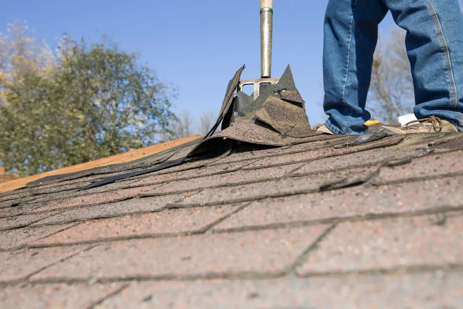 Damaged asphalt roof shingles with patches and wear exposed on the roof surface