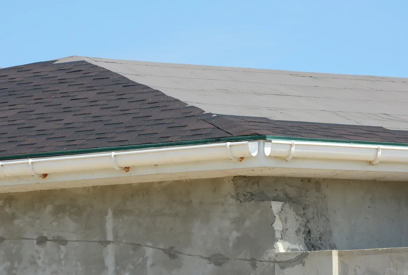 Worker using a yellow nail gun to install shingles on a roof beside a ladder